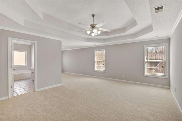 unfurnished room with light carpet, a tray ceiling, a wealth of natural light, and visible vents