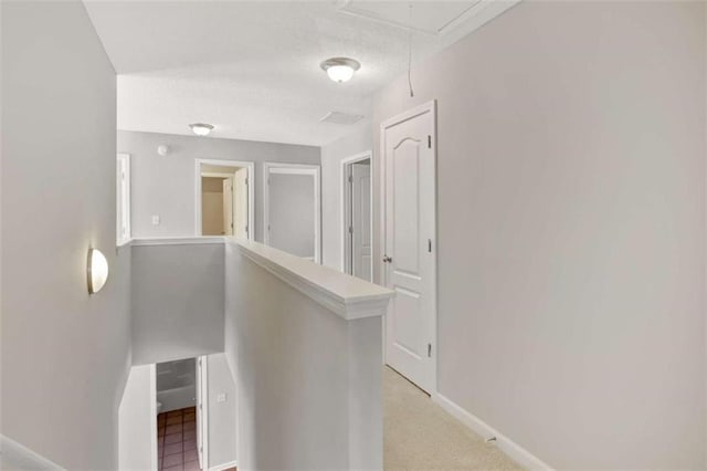 hallway featuring attic access, baseboards, a textured ceiling, and an upstairs landing