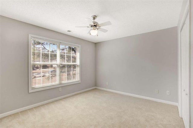 spare room with light carpet, a textured ceiling, baseboards, and a ceiling fan