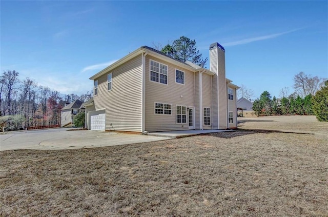 back of property featuring a garage, driveway, a yard, a chimney, and a patio area