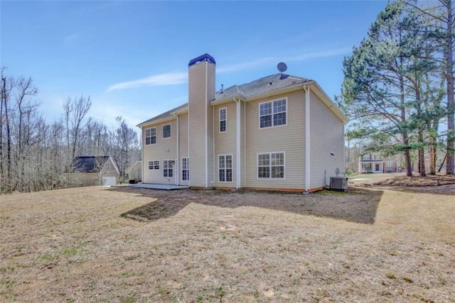 back of house with central AC, a yard, and a chimney