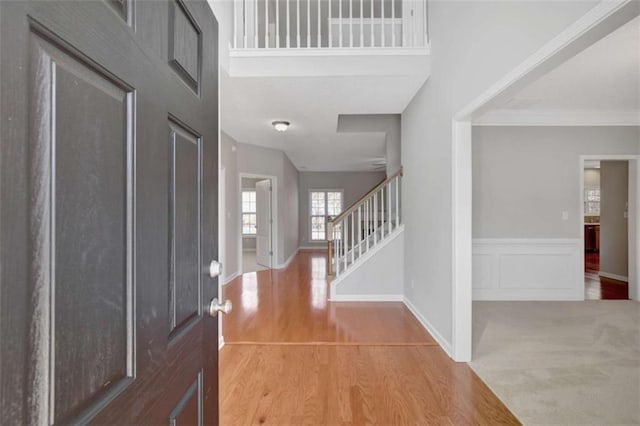 foyer entrance with a decorative wall, wood finished floors, stairs, ornamental molding, and wainscoting