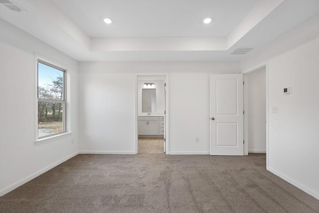 unfurnished bedroom with carpet flooring, connected bathroom, and a raised ceiling