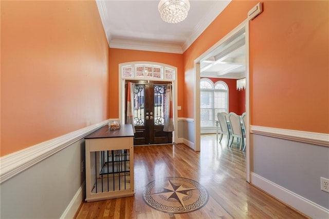 entrance foyer with crown molding, wood-type flooring, french doors, and a notable chandelier