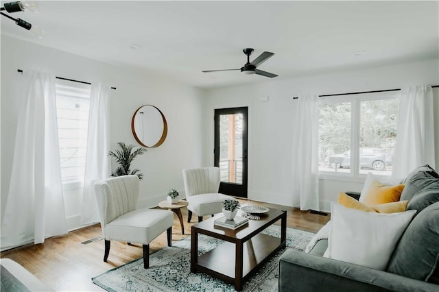 living area with light wood finished floors, a ceiling fan, and baseboards