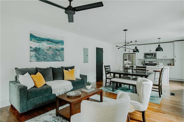 living room with electric panel, a ceiling fan, and light wood-style flooring