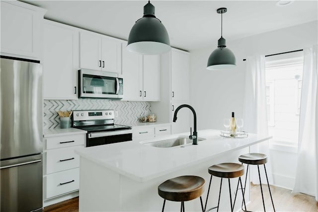 kitchen featuring appliances with stainless steel finishes, a sink, a center island with sink, tasteful backsplash, and a breakfast bar area