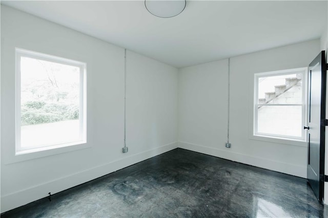 spare room featuring plenty of natural light, concrete floors, and baseboards