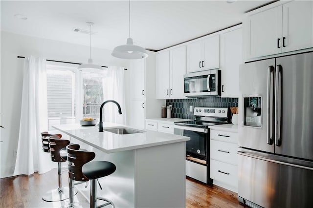 kitchen featuring stainless steel appliances, a sink, light countertops, backsplash, and wood finished floors