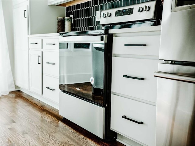 kitchen view of stainless steel range with electric stovetop, wood finished floors, and white cabinetry