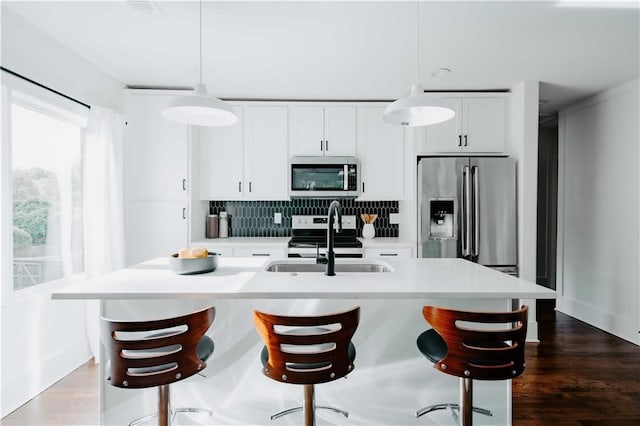 kitchen featuring stainless steel appliances, a sink, backsplash, a kitchen island with sink, and light countertops