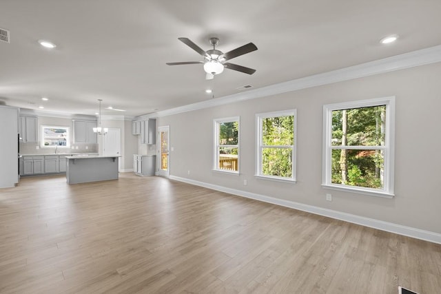 unfurnished living room with ceiling fan with notable chandelier, light hardwood / wood-style flooring, and ornamental molding