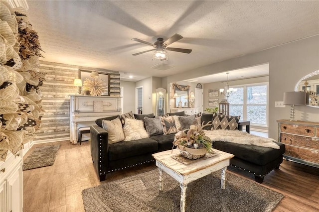 living room with ceiling fan with notable chandelier, hardwood / wood-style floors, a textured ceiling, and wood walls