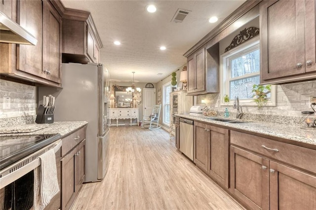 kitchen with light stone countertops, appliances with stainless steel finishes, sink, and light wood-type flooring