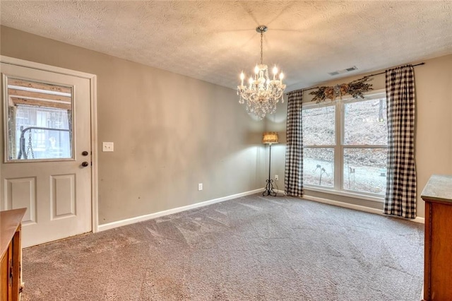 carpeted spare room with a chandelier and a textured ceiling