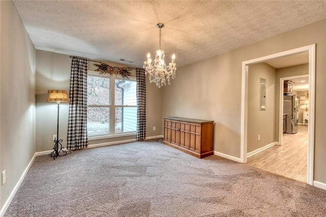 empty room featuring a chandelier, carpet flooring, electric panel, and a textured ceiling