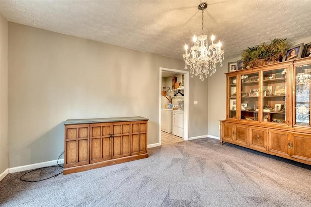 unfurnished dining area featuring washing machine and clothes dryer, a chandelier, light colored carpet, and a textured ceiling