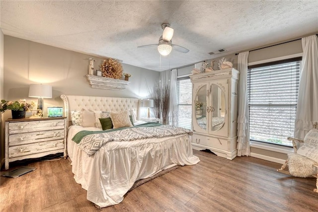 bedroom with multiple windows, a textured ceiling, wood-type flooring, and ceiling fan