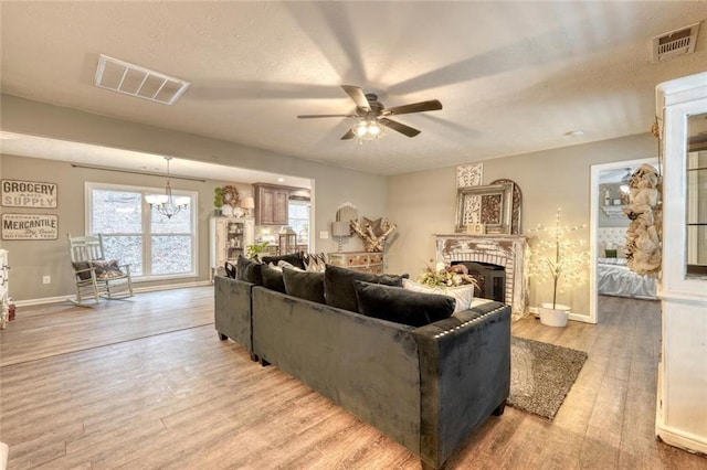 living room featuring a fireplace, ceiling fan with notable chandelier, light hardwood / wood-style flooring, and a textured ceiling