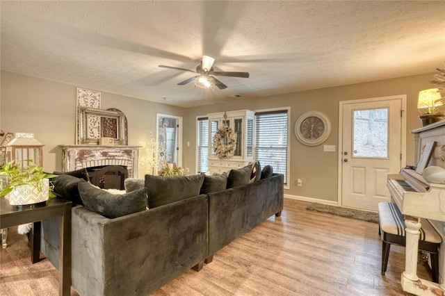 living room with ceiling fan, a fireplace, a textured ceiling, and light wood-type flooring