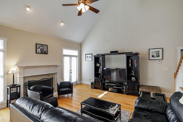 living area with light wood-style floors, a high end fireplace, high vaulted ceiling, baseboards, and stairs