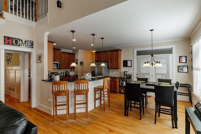 kitchen with a peninsula, a breakfast bar, appliances with stainless steel finishes, light wood finished floors, and dark countertops