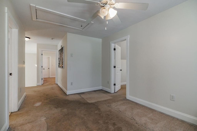 carpeted empty room with ceiling fan, attic access, and baseboards