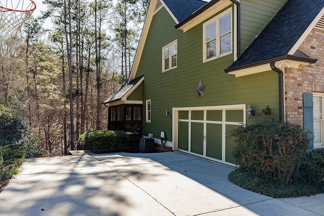 view of side of property featuring an attached garage, brick siding, a shingled roof, and central air condition unit