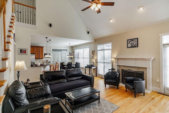 living area featuring light wood-style floors, a high end fireplace, ceiling fan, high vaulted ceiling, and baseboards