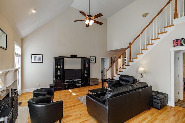 living room with baseboards, wood finished floors, stairs, a fireplace, and high vaulted ceiling