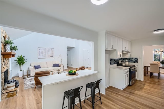 kitchen featuring gas range, a kitchen breakfast bar, tasteful backsplash, kitchen peninsula, and white cabinets