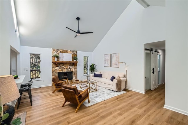 living room featuring a barn door, light hardwood / wood-style flooring, high vaulted ceiling, and a fireplace