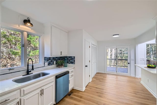 kitchen with light wood-type flooring, tasteful backsplash, sink, dishwasher, and white cabinetry