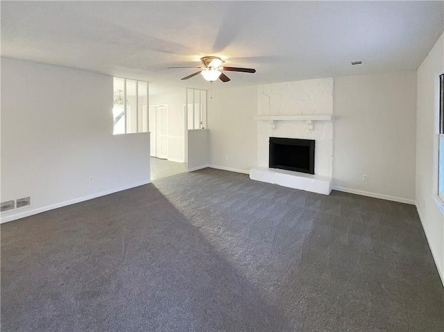 unfurnished living room with ceiling fan, a large fireplace, and dark colored carpet