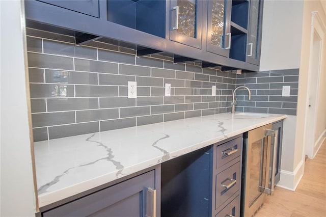 kitchen with backsplash, light stone counters, sink, light hardwood / wood-style flooring, and wine cooler