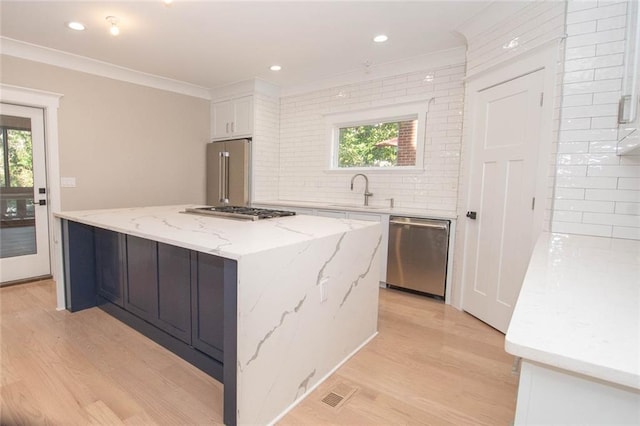 kitchen featuring light stone countertops, appliances with stainless steel finishes, sink, white cabinets, and a center island