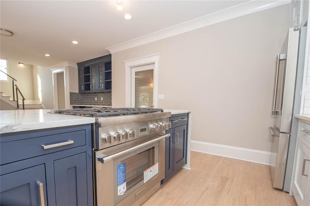 kitchen featuring high end appliances, light stone countertops, tasteful backsplash, light wood-type flooring, and ornamental molding