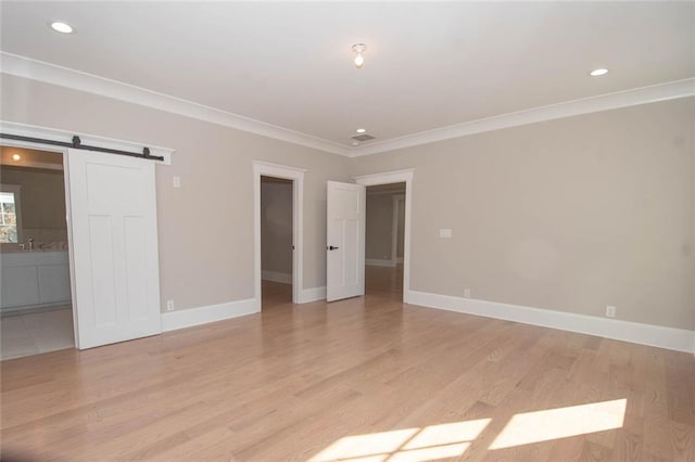 interior space featuring a barn door, light hardwood / wood-style floors, and ornamental molding