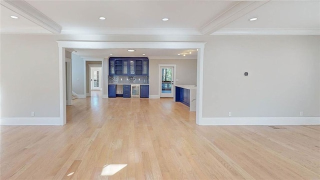 unfurnished living room featuring beam ceiling, light wood-type flooring, and ornamental molding