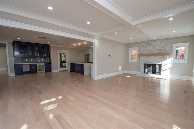 unfurnished living room with coffered ceiling, crown molding, hardwood / wood-style flooring, beamed ceiling, and a stone fireplace