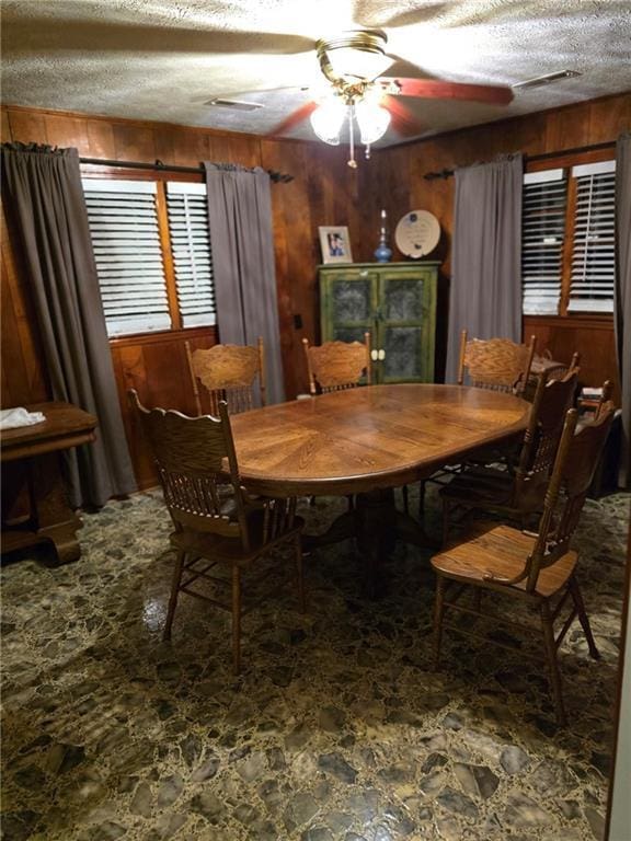 dining room with ceiling fan, a textured ceiling, and wood walls