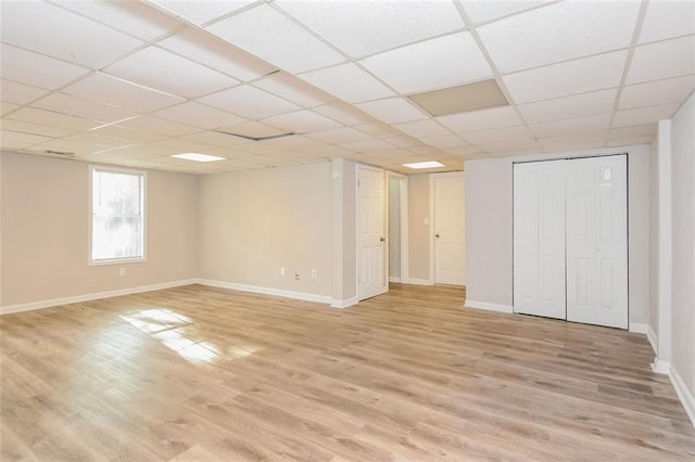 basement featuring a paneled ceiling and light hardwood / wood-style flooring