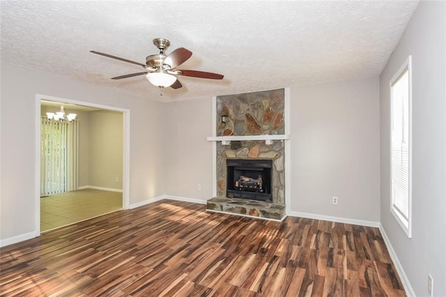 unfurnished living room with a healthy amount of sunlight, ceiling fan with notable chandelier, dark hardwood / wood-style floors, and a stone fireplace