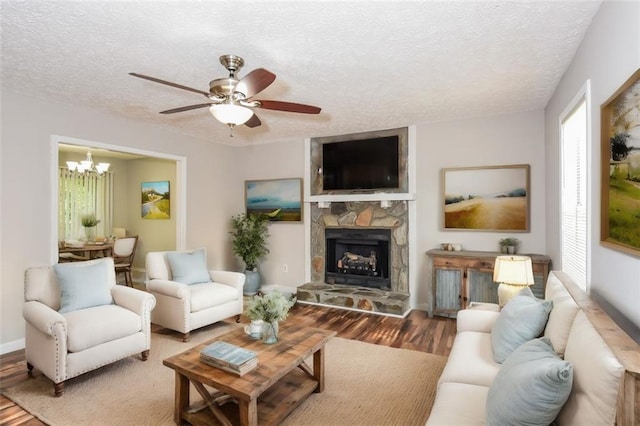 living room featuring ceiling fan with notable chandelier, hardwood / wood-style flooring, a textured ceiling, and a stone fireplace