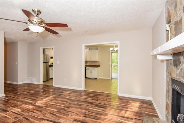 unfurnished living room with ceiling fan with notable chandelier, a textured ceiling, hardwood / wood-style floors, and a stone fireplace