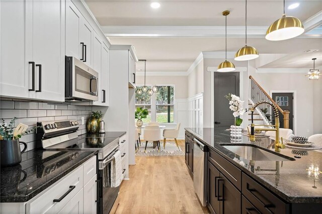 kitchen with light wood finished floors, a sink, appliances with stainless steel finishes, and ornamental molding