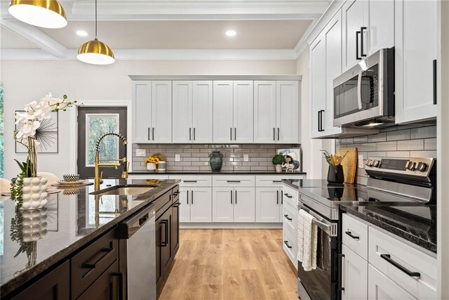 kitchen featuring dark stone counters, a sink, light wood-style floors, appliances with stainless steel finishes, and decorative light fixtures