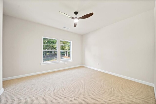 carpeted spare room featuring baseboards, visible vents, and ceiling fan