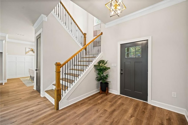 entrance foyer featuring an inviting chandelier, stairway, wood finished floors, and crown molding