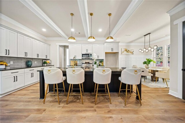 kitchen with dark countertops, stainless steel microwave, light wood-type flooring, and beam ceiling
